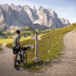 Osoba z rowerem stoi przy rozwidleniu górskich tras w dolinie Dolomitów.