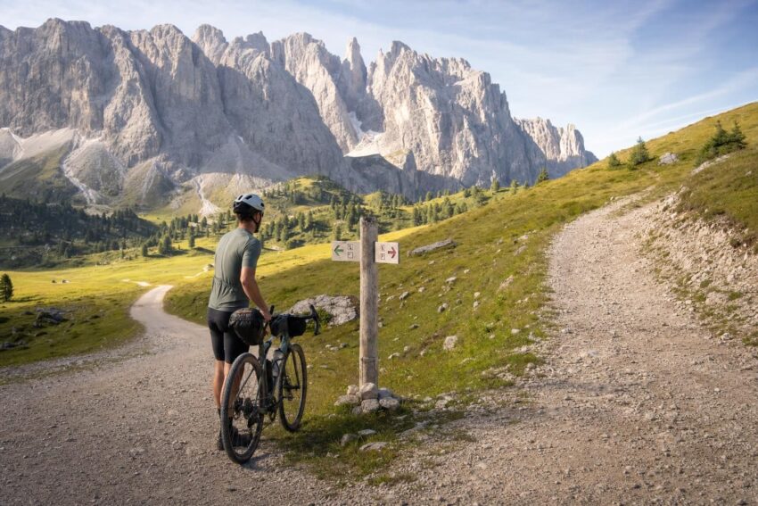 Osoba z rowerem stoi przy rozwidleniu górskich tras w dolinie Dolomitów.
