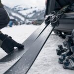 Osoba sprawdza używane narty i buty na śniegu przy samochodzie zimą