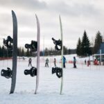 Trzy snowboardy ustawione w śniegu przy łagodnym stoku, pokazujące różne profile desek.