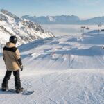 Osoba ocenia snowpark i stok snowboardowy w austriackim ośrodku zimowym.