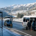 Zimowy dojazd do ośrodka narciarskiego: bus, auto i osoby z nartami w górskiej dolinie.
