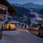 Pensjonat przy ośnieżonej drodze w alpejskiej miejscowości, stok i przystanek ski busu w oddali
