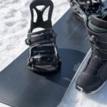 Zbliżenie na snowboard i but ustawiony obok na śniegu dla porównania szerokości.