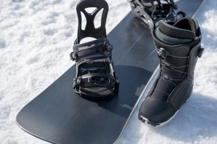 Zbliżenie na snowboard i but ustawiony obok na śniegu dla porównania szerokości.