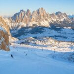 Ośnieżone stoki i szczyty Dolomitów o poranku, z kilkoma narciarzami w oddali