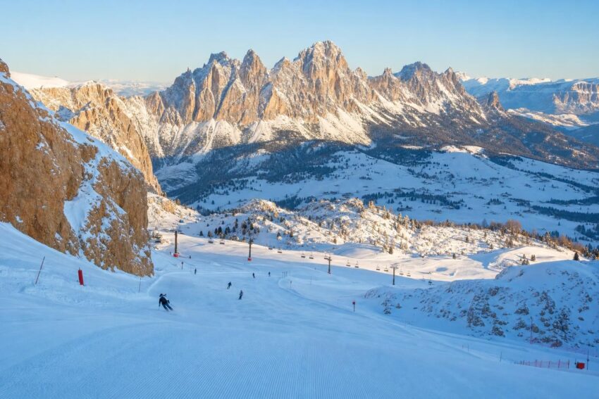 Ośnieżone stoki i szczyty Dolomitów o poranku, z kilkoma narciarzami w oddali