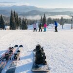 Narty i snowboard obok siebie na śniegu przy łagodnym stoku dla początkujących.