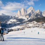 Łagodny stok narciarski w Dolomitach, osoba przy mapie tras i alpejska miejscowość w tle