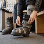 Osoba siedzi na ławce i dopasowuje buty narciarskie w jasnym punkcie fittingowym.