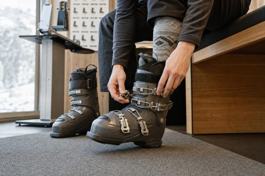 Osoba siedzi na ławce i dopasowuje buty narciarskie w jasnym punkcie fittingowym.