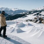 Osoba stoi przy stoku i ocenia snowpark w szwajcarskim ośrodku na tle gór.