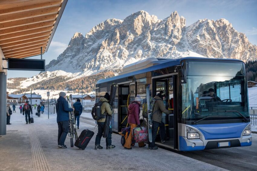 Osoba z nartami wsiada do ski busa przy ośnieżonym przystanku w Dolomitach.