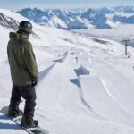 Snowpark w Alpach Francuskich z przeszkodami i osobą oceniającą trasę na snowboard