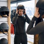 Osoba porównuje kask narciarski przed lustrem w sklepie sportowym.