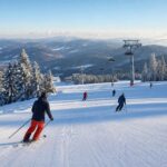 Szeroki widok na ośrodek narciarski w Polsce, przygotowany stok, kilku narciarzy i wyciąg zimą